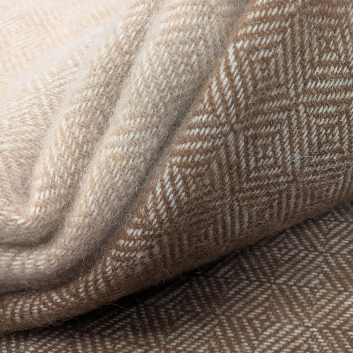 A close-up of folded woven alpaca textiles with both fawn and cream, and brown and cream geometric diamond patterns