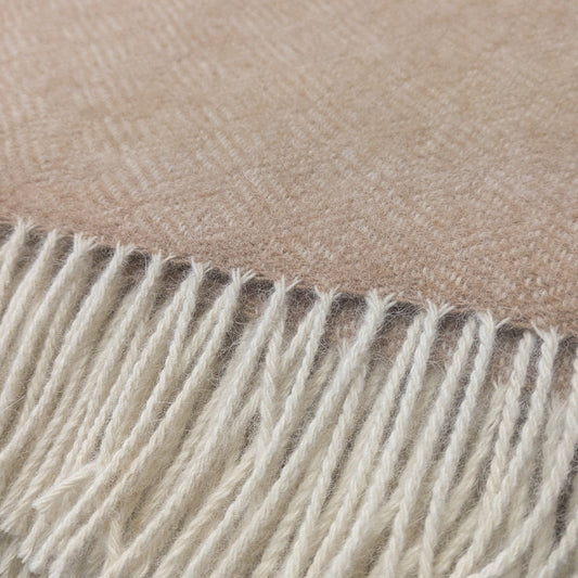 A close-up of a woven cream alpaca blanket throw with cream fringe along one edge.