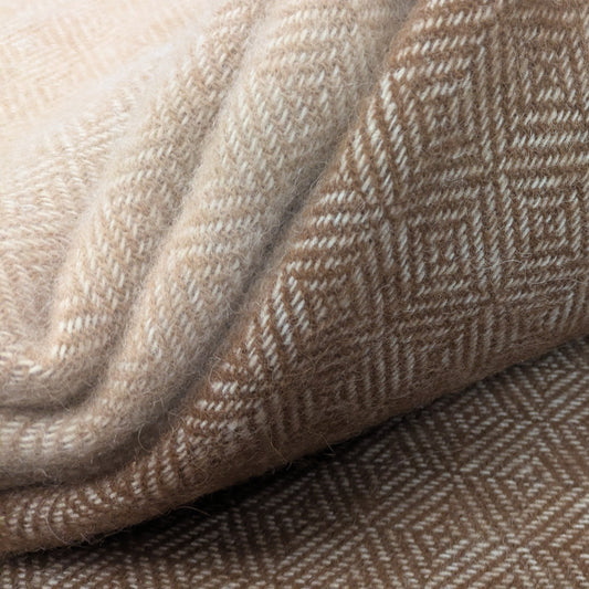 A close-up of folded woven alpaca textiles with both fawn and cream, and brown and cream geometric diamond patterns